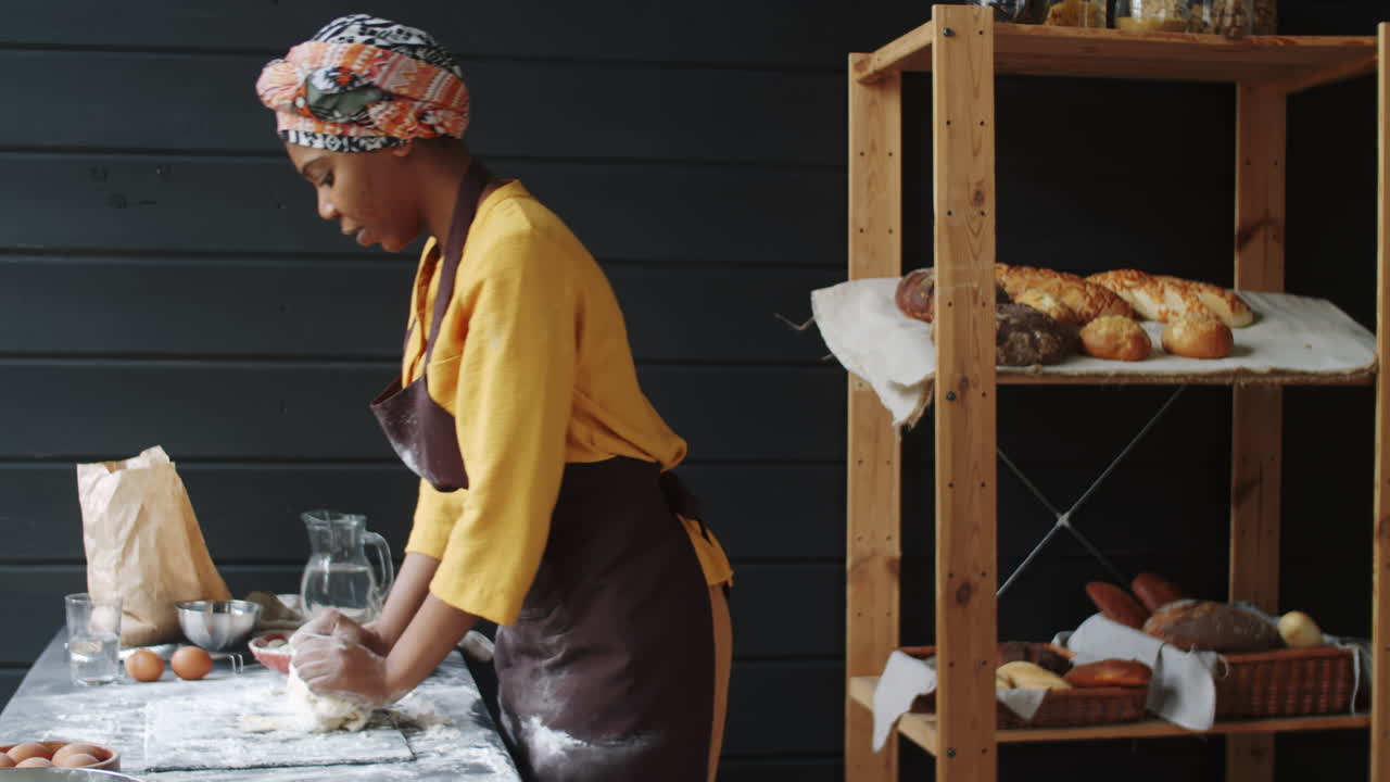 African American Woman in Apron Kneading Dough in Bakery