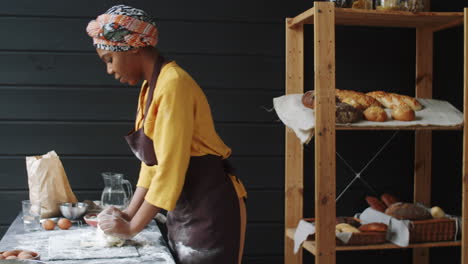 african american woman in apron kneading dough in bakery