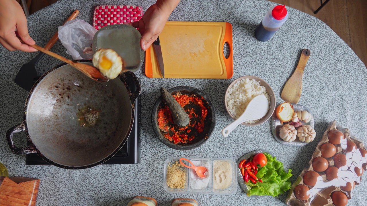Pemandangan dari atas koki menggoreng telur di wajan panas berisi minyak, membaliknya menggunakan piring kecil