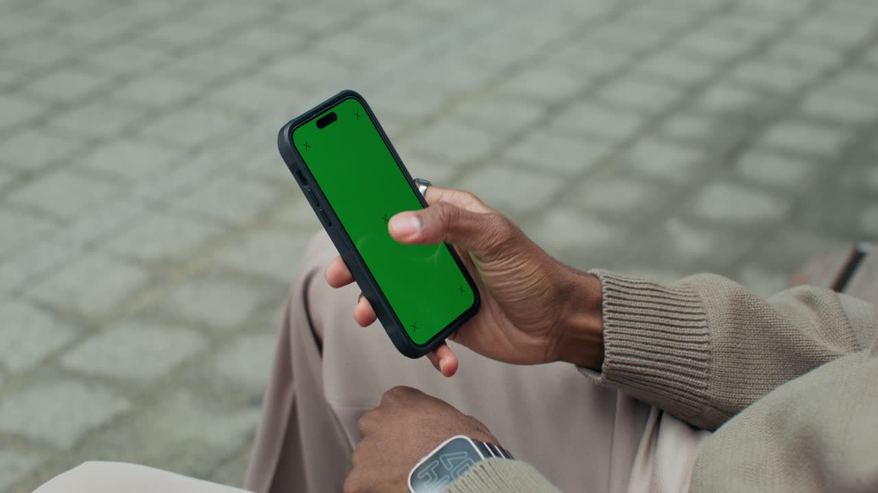 Person holding a smartphone with a green screen outdoors