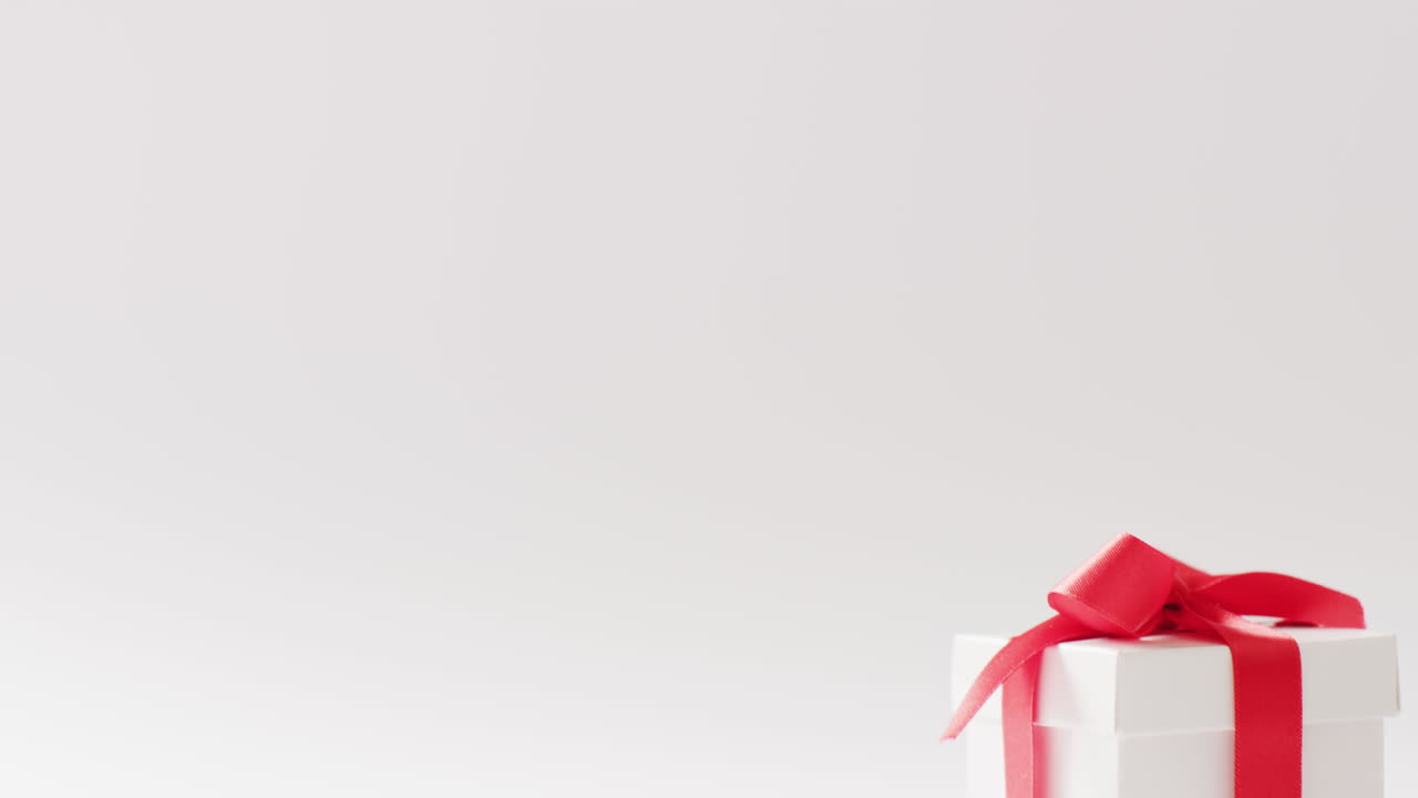 vista lateral de video de una caja de regalo blanca atada con cinta roja, sobre fondo blanco con espacio de copia