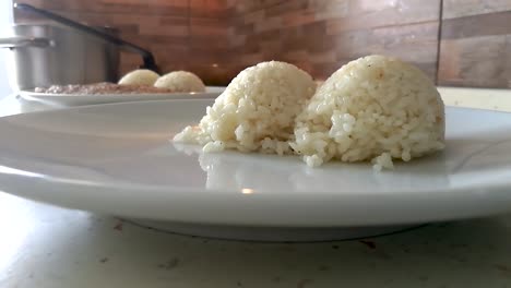 chef emplatando bolas de arroz blanco humeante en un plato redondo con un cucharón de plástico