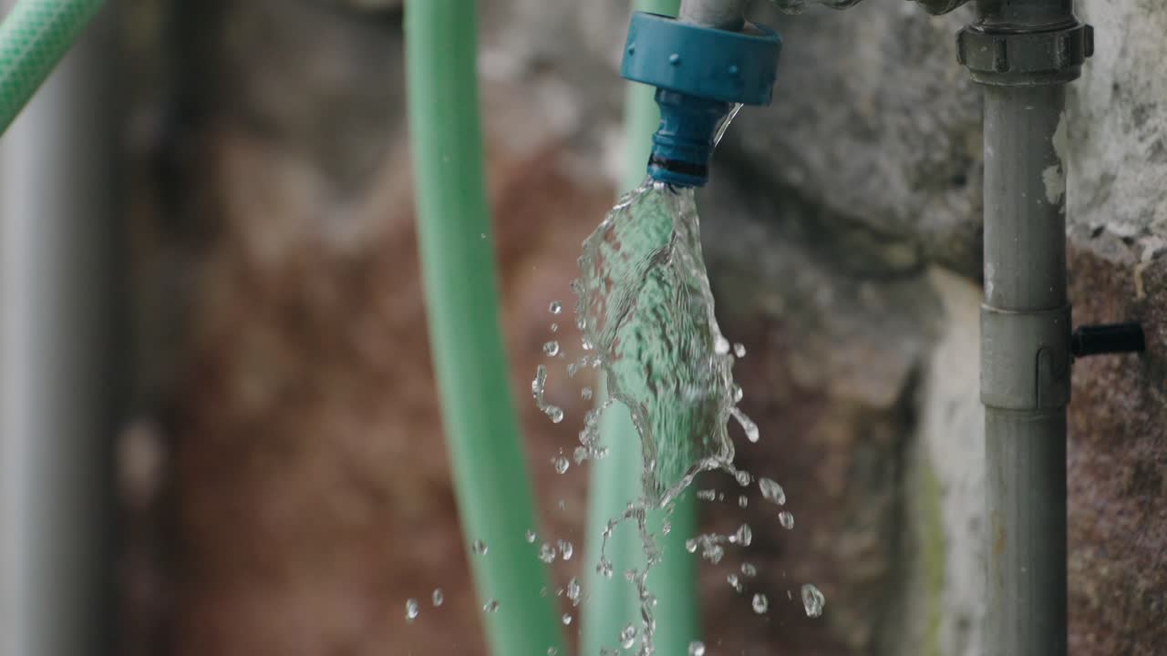 Close up of water splashing from a green hose against a stone wall