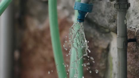 close up of water splashing from a green hose against a stone wall