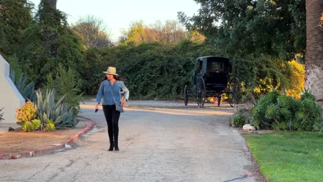 Mujer-Hispana-Alejándose-Del-Carruaje-Antiguo-En-El-Museo-Rancho-Camulos,-Tarde-Soleada