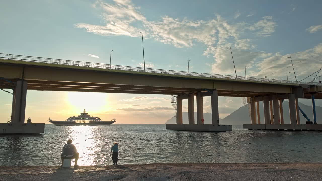 Peaceful Golden hour fishing scene as Greek ferry crosses bay of Corinth bridge