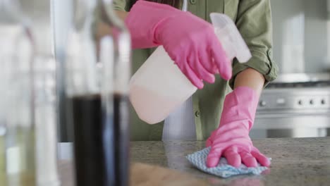 mujer caucásica con guantes de goma y mesa de limpieza en casa