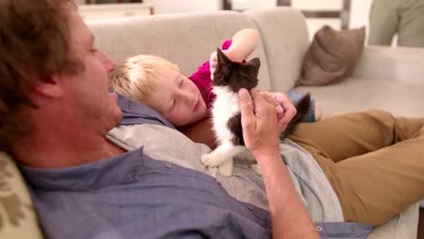 modern dad holding cat for son to pet on couch