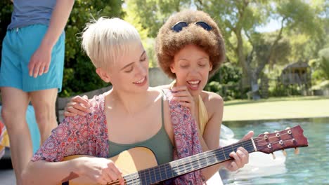 happy diverse group of friends playing guitar at pool party in summer