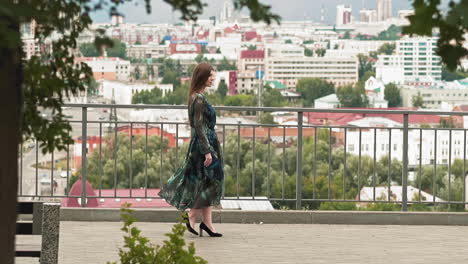 Elegant-woman-in-long-dress-walks-on-viewpoint-against-city