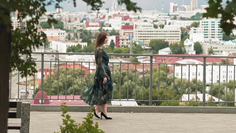 elegant woman in long dress walks on viewpoint against city