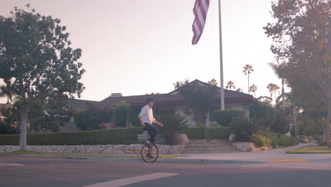 A person rides a unicycle in front of an American flag
