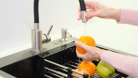 caring young woman with little female child washing fresh fruits in kitchen sink