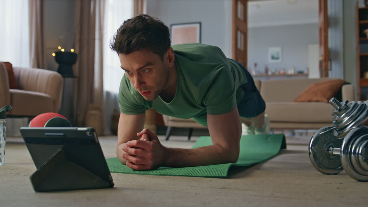 Athlete looking video tutorial by tablet in apartment. Fit man training online