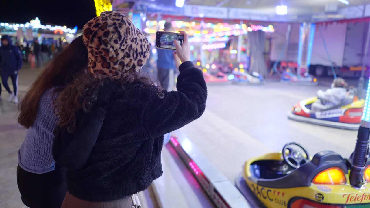 Girls taking photos at a funfair at night