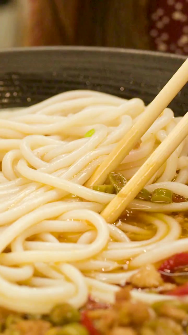 スパイシーなスープの中で、木製の箸と黒いスプーンが太い麺を混ぜている超クローズアップ。