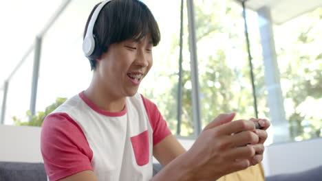 teenage asian boy enjoys gaming on smartphone at home