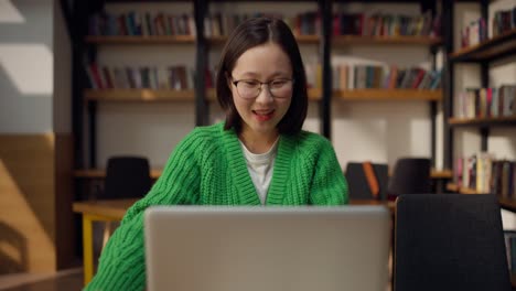 mujer estudiando en una biblioteca con una computadora portátil