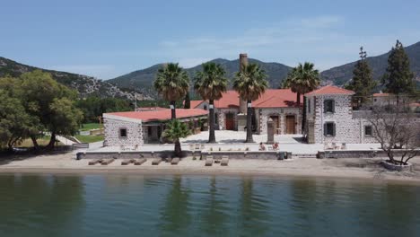 tourist couple sunbathing in outdoor area of an isolated hotel property with private beach, zaira hotel beautiful landscape surrounding hills and olive gardens, lesvos island, drone shot