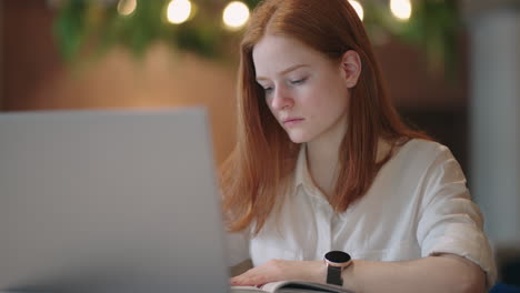 young woman is learning remote viewing tutorial on laptop display and writing notes in book