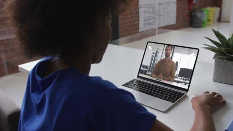 Back-view-of-african-american-woman-having-a-video-call-with-male-colleague-on-laptop-at-office