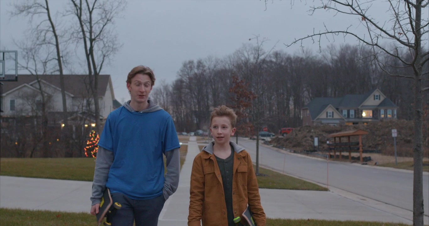 two young boys walk toward the camera holding skateboards and talking