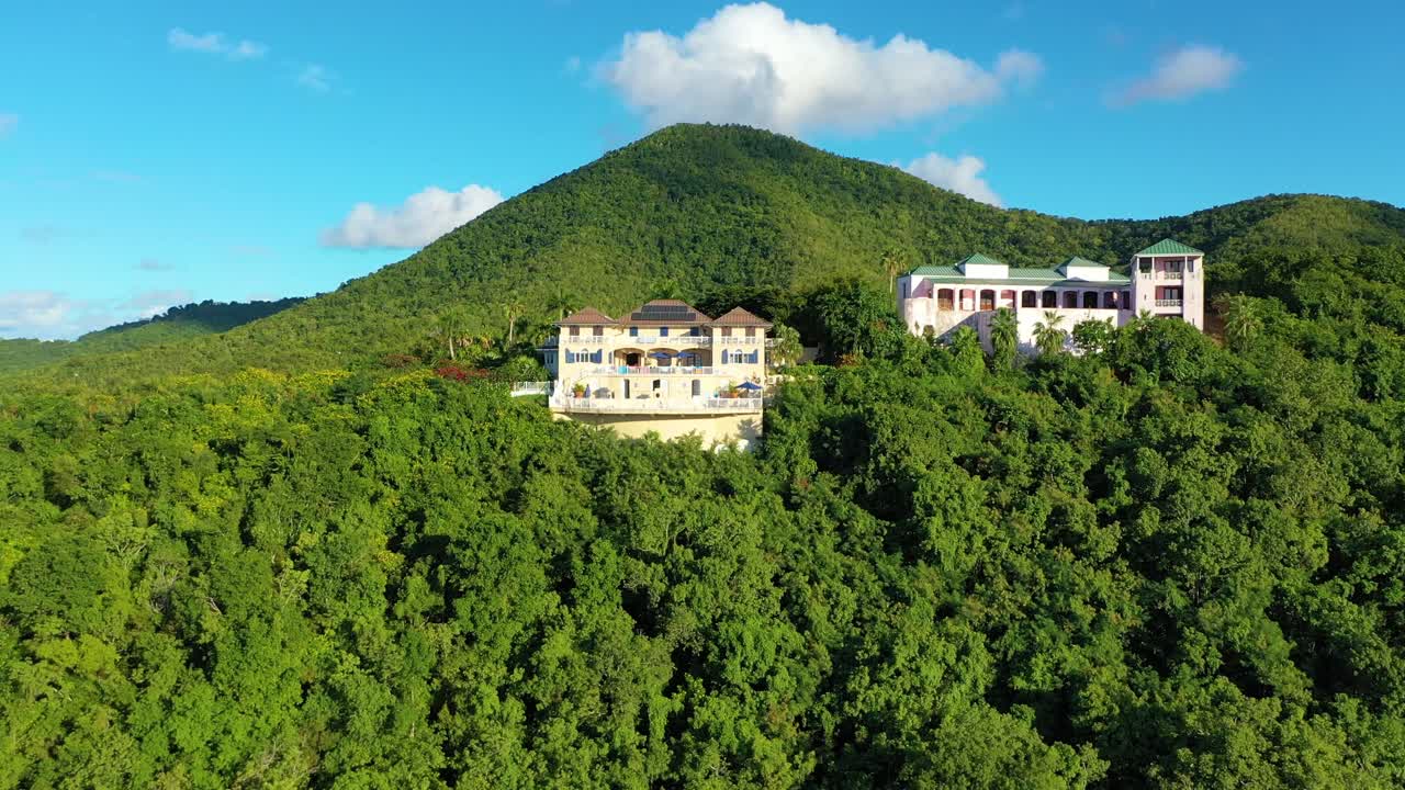 Aerial view of St. Croix reveals elegant villas nestled among tropical trees, scattered across green hills with forested ridges and misty island mountains climbing gently into a sunlit sky