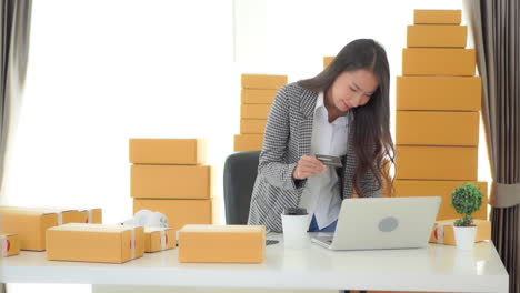 a young, pretty, asian woman stands over her desk as she enters her credit card number online