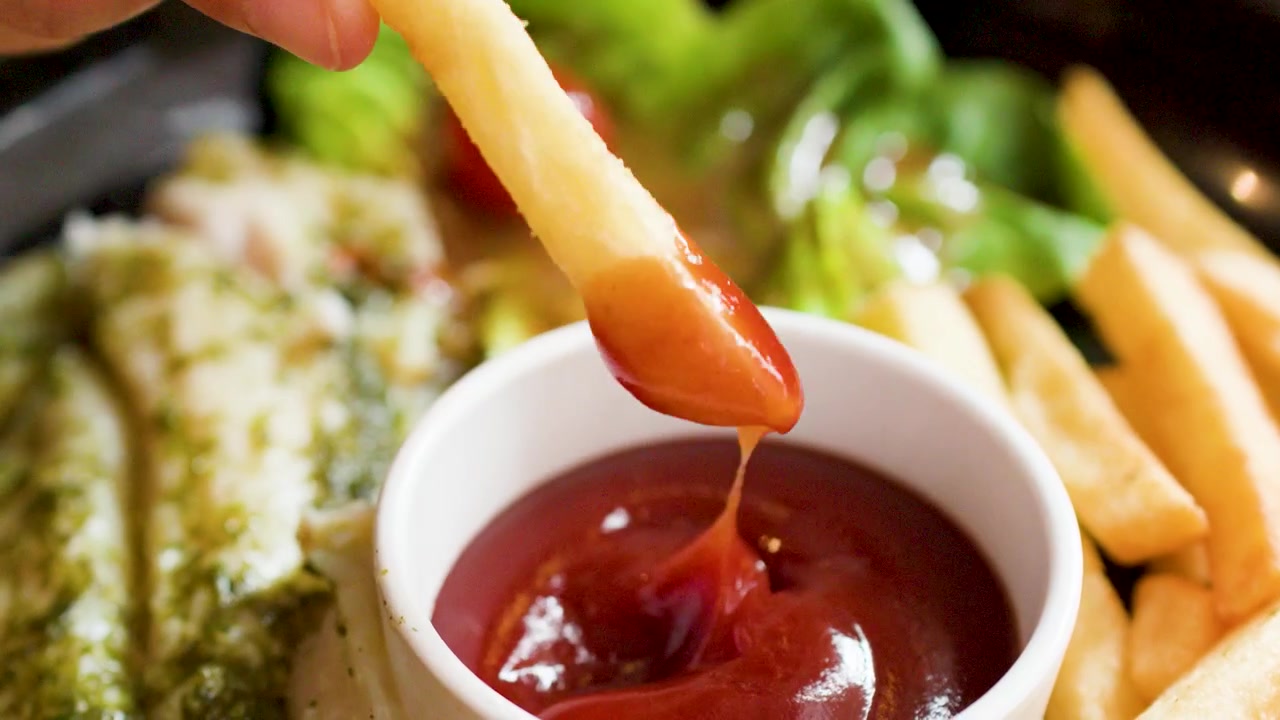 Eine Hand taucht eine knusprige Pommes frites in eine Schale mit roter Tomatenketchup-Soße.