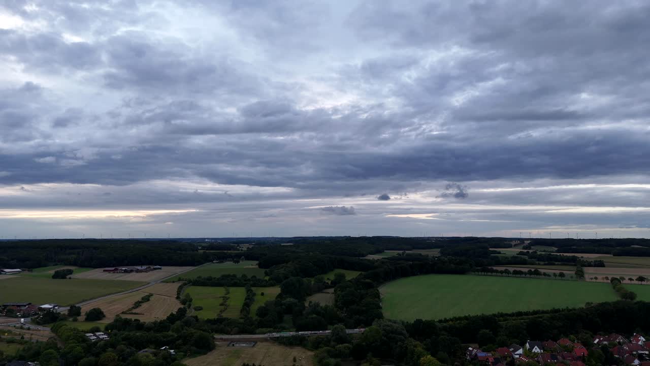 Agricultural farm fields in different colors on hillside of American town. Suburb neighborhood, interstate road and forest trees on cloudy summer day in rural district. Aerial wide shot