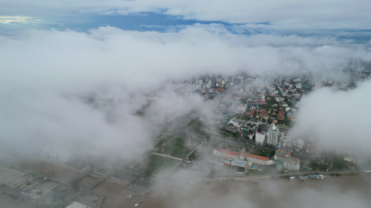 Aerial video of Phnom Penh shows city buildings peeking through thick low clouds, with the brown waters of the Tonle Sap River faintly visible below