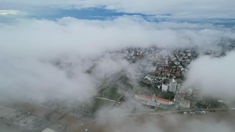 aerial video of phnom penh shows city buildings peeking through thick low clouds, with the brown waters of the tonle sap river faintly visible below