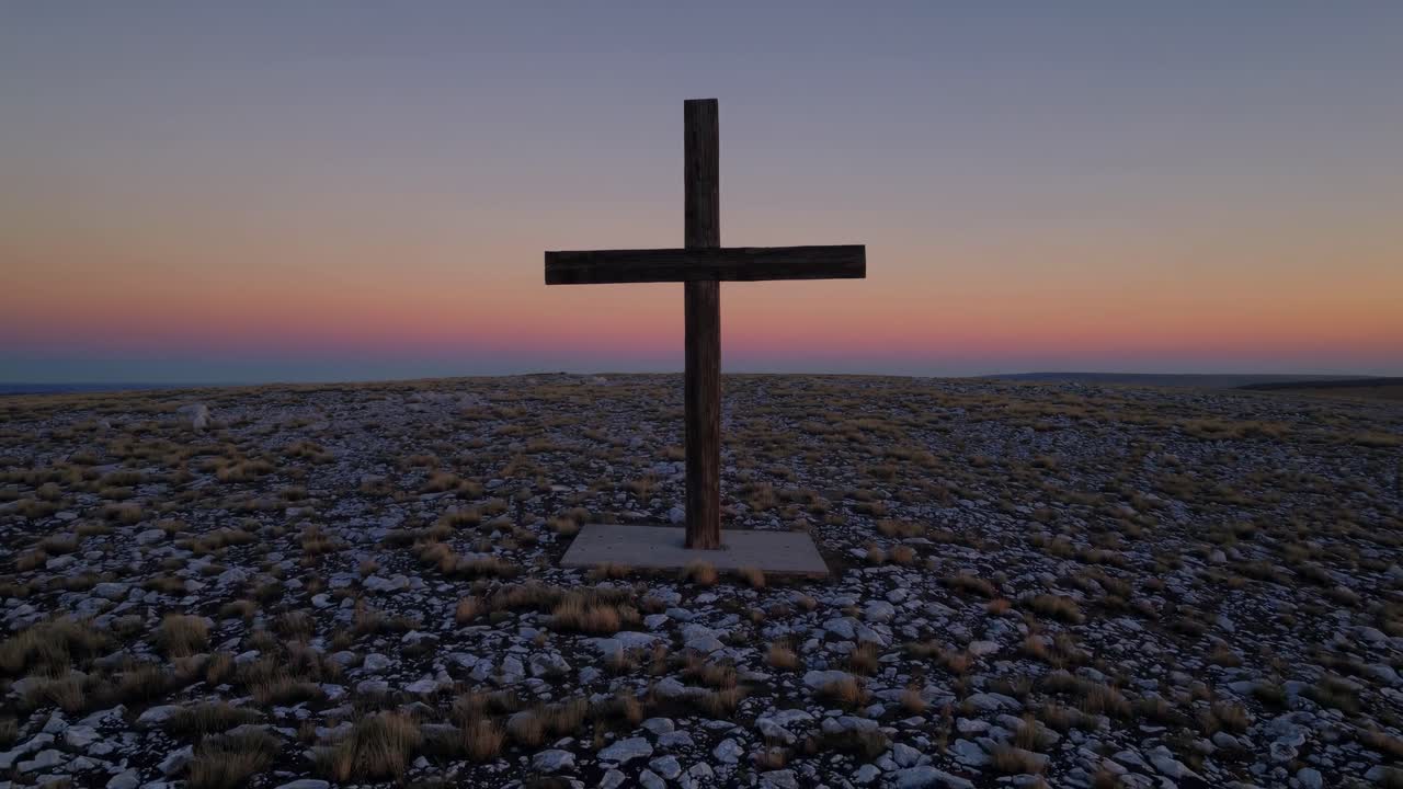 Video aéreo captura una cruz solitaria en una colina rocosa al atardecer, enfatizando la soledad.