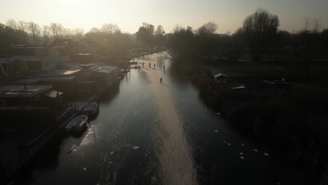 Aerial-Sillhouute-View-Of-Locals-Ice-Skating-Over-Frozen-Canals-In-Hendrik-Ido-Ambacht-With-Warm-Winter-Sun-Overhead