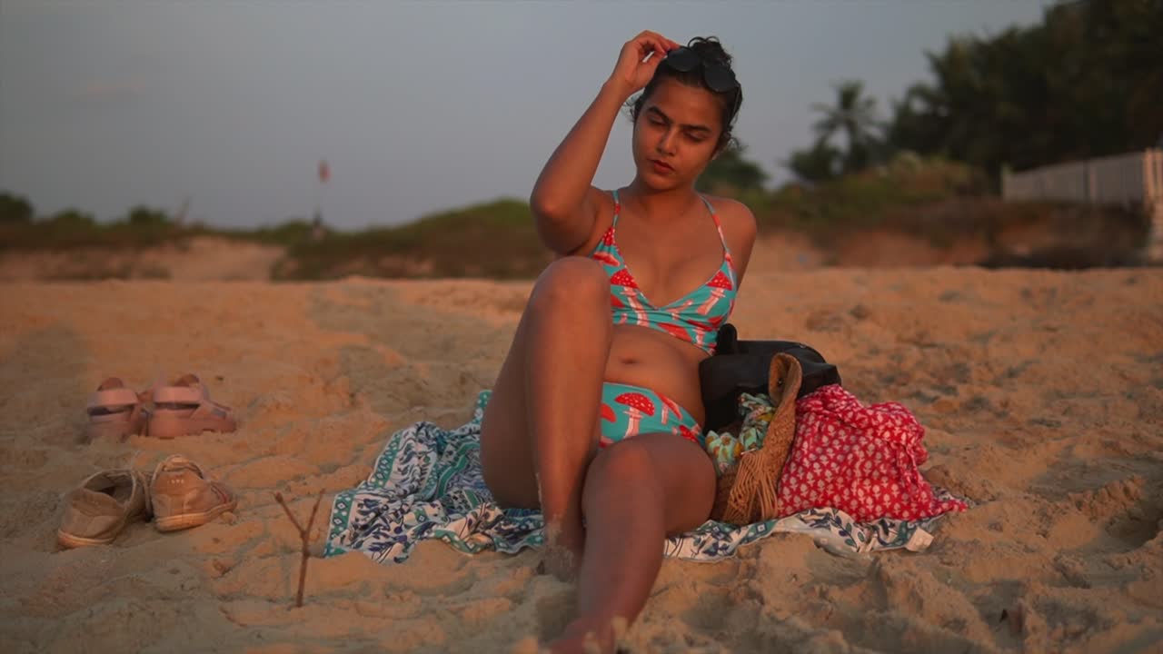 Young brunette woman or girl in a swimsuit lying on the sand on the beach at sunset