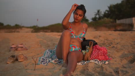 Young-brunette-woman-or-girl-in-a-swimsuit-lying-on-the-sand-on-the-beach-at-sunset