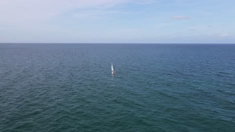 Aerial-flight-to-white-sailboat-alone-on-flat-calm-blue-Atlantic-ocean