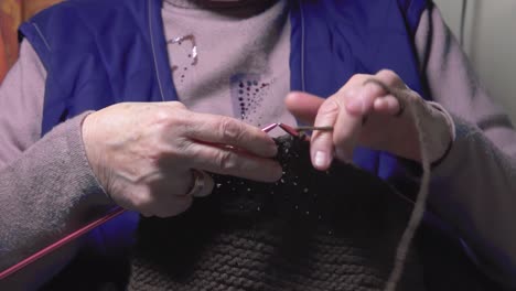 old adult woman holding needles knitting knitwear scarf relaxing on sofa