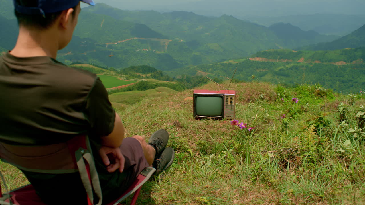 Amidst nature's beauty, a man watches an old TV sparking contemplation