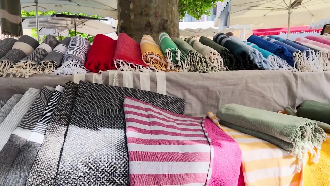 Una lenta panoramica attraverso coperte e asciugamani colorati piegati in un mercato all'aperto soleggiato.