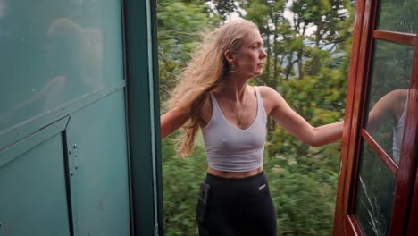 a woman on the open door of a moving train along the iconic ella to kandy route in sri lanka, taking in the breathtaking views of green hills, tea plantations, and dense jungle.