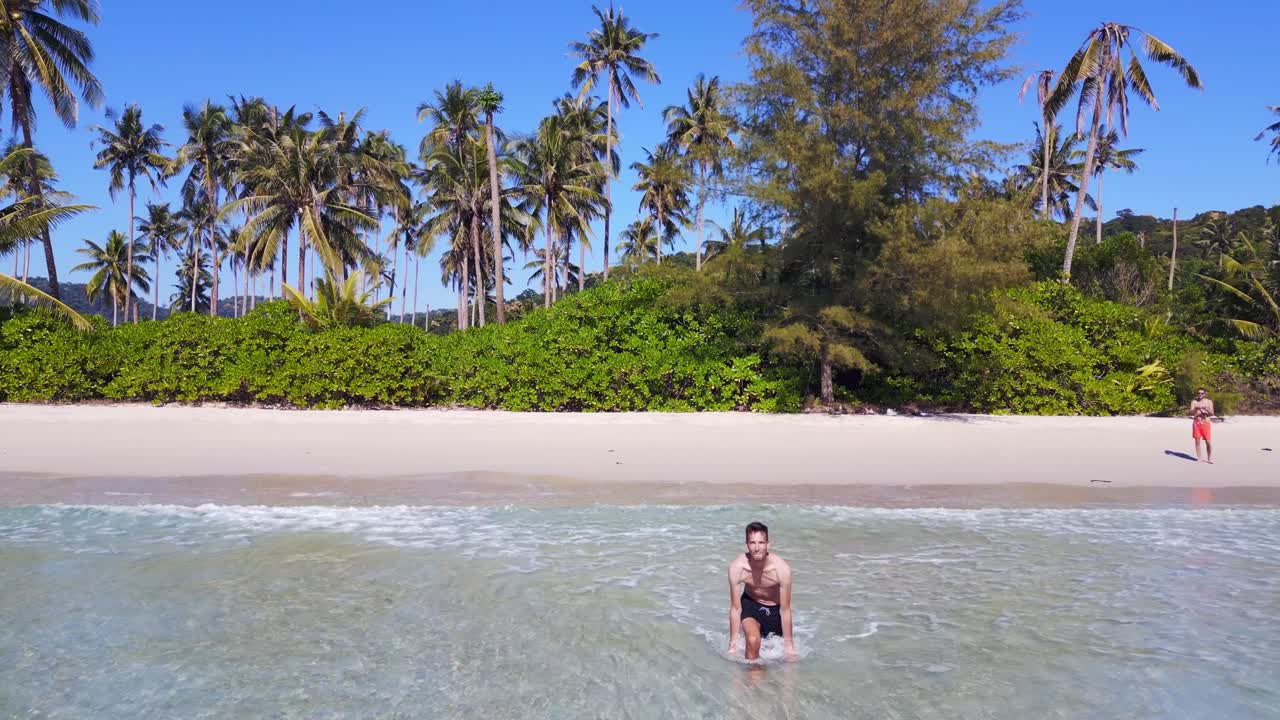 Man walks into crystal clear turquoise sea, splashes with water