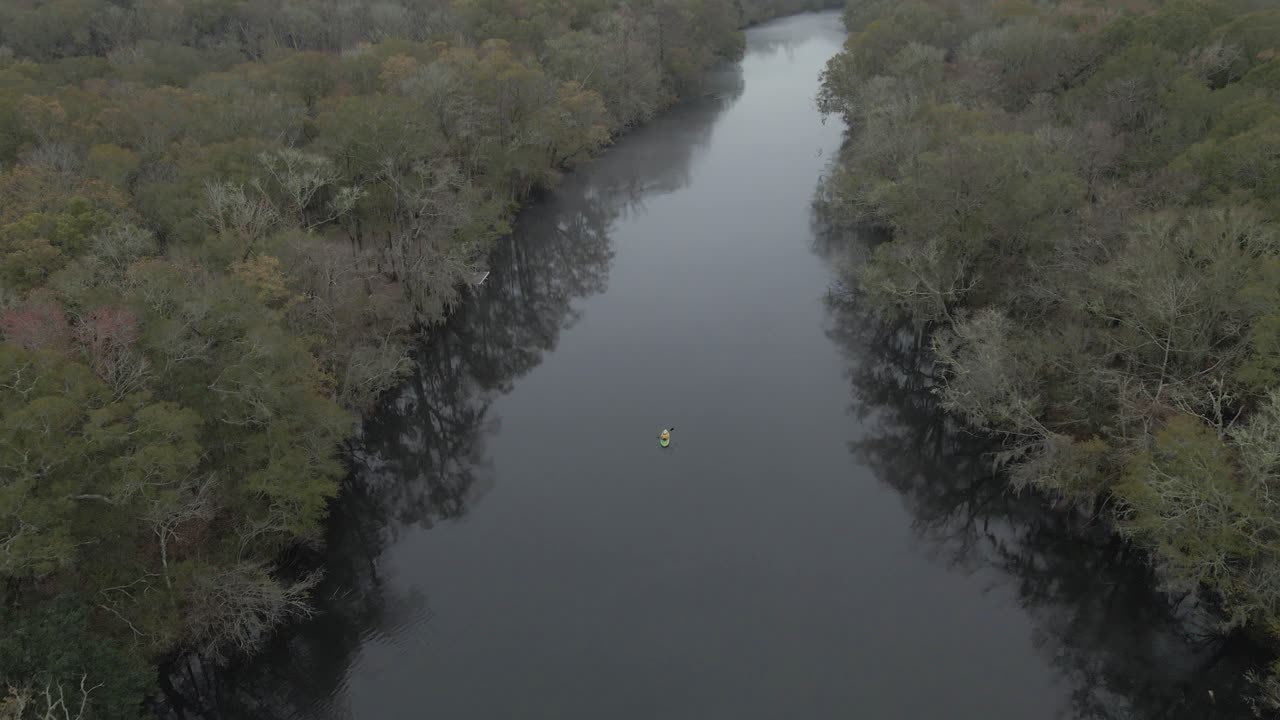 green kayak slowly paddling in the center of a calm river on a overcast day in Edisto