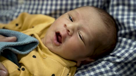 newborn baby boy in yellow onesie yawning or crying on checkered blanket, close-up