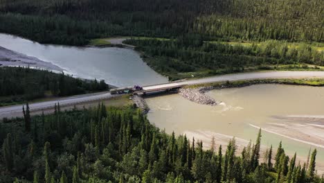 Big-fuel-tanker-truck-shipping-fuel-on-the-countryside-road,-crossing-bridge-and-drives-by-the-river-at-Alaska,-Deadhorse---aerial-following-shot