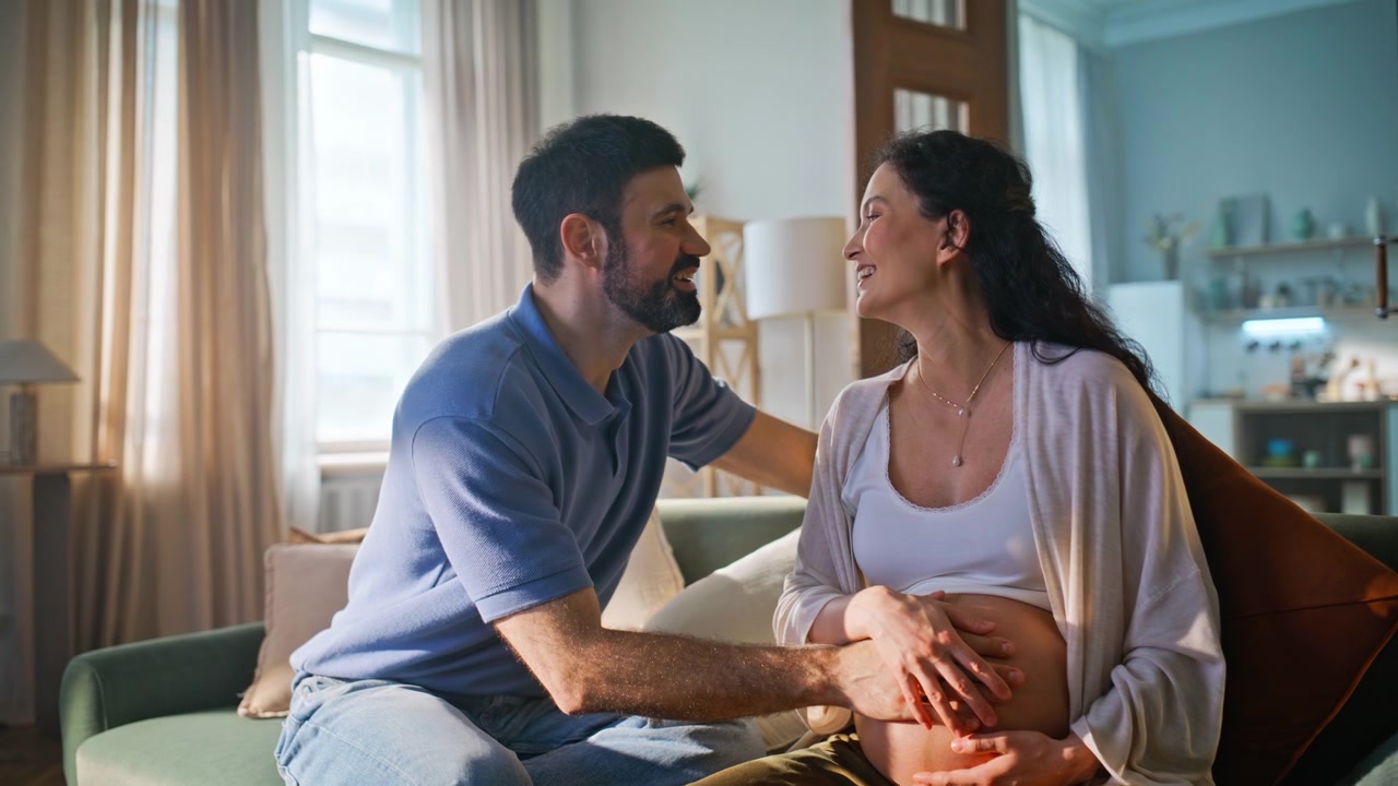 Couple expecting baby touching pregnant belly home. Loving husband bonding wife.