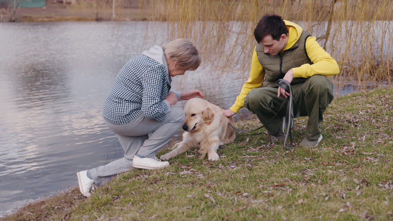 Senior and Young Adult with Golden Retriever by a Pond