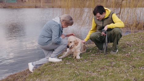 senior and young adult with golden retriever by a pond