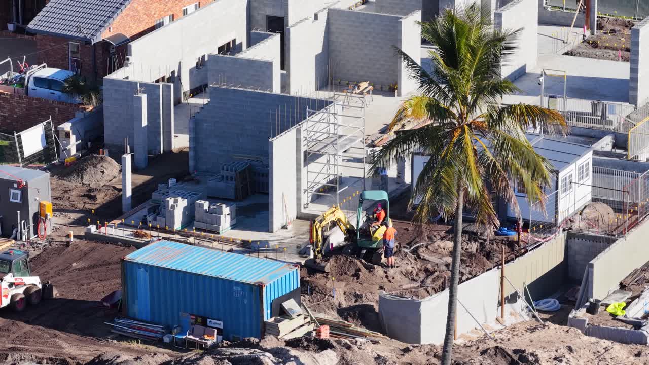 Drone footage captures workers and machinery at a construction site under bright daylight in Gold Coast, Australia