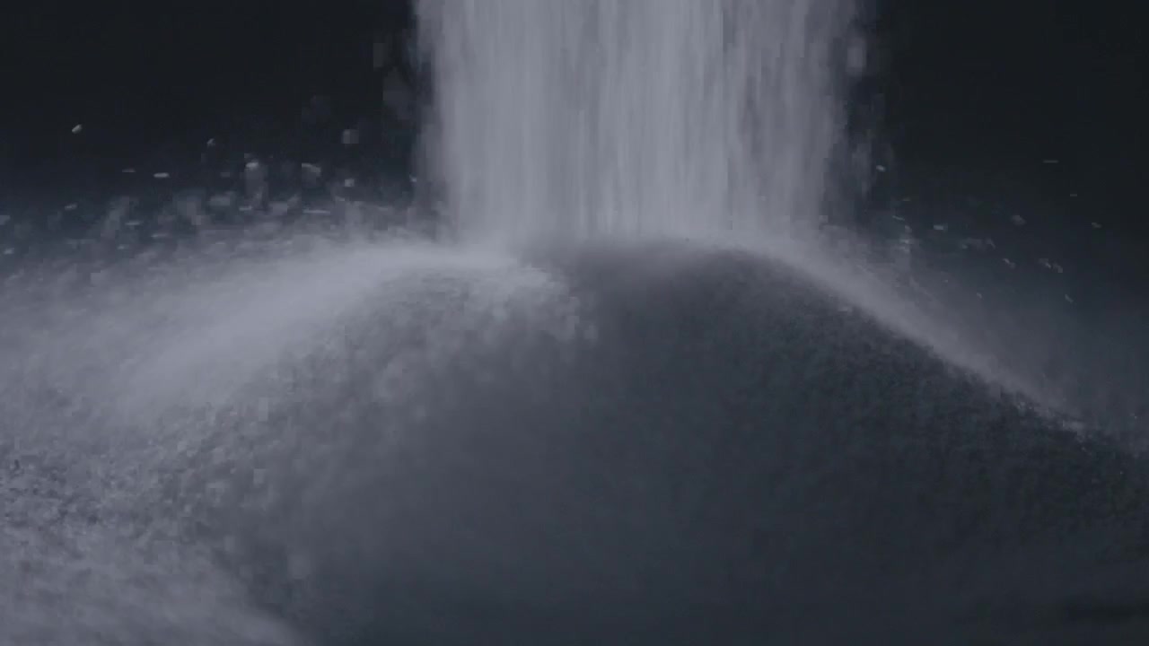 Zucchero fine che cade a cascata con grazia al rallentatore su uno sfondo scuro con particelle sparse.